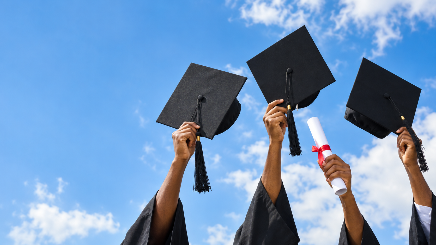 Graduation caps and a diploma raised against a bright blue sky